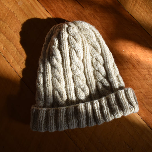 Knitted gray beanie on a wooden floor with sunlight casting shadows