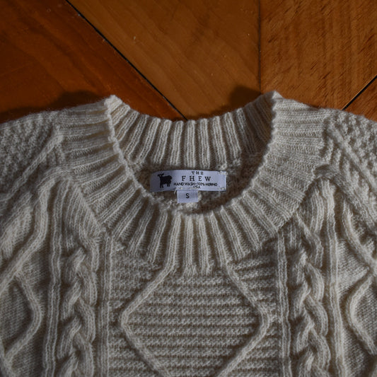 Beige cable knit sweater with a brand label on a wooden floor