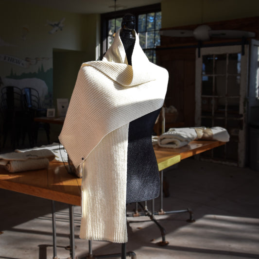 Mannequin wearing a cream-colored merino wool scarf in a room with tables and chairs.