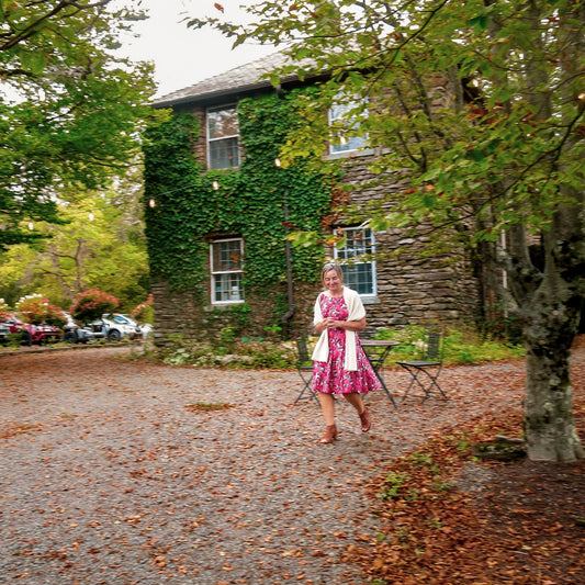 Woman standing in front of a stone building covered in ivy with cars parked nearby.