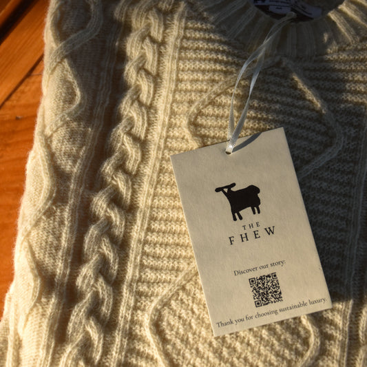 Beige cable knit sweater with a tag on a wooden surface
